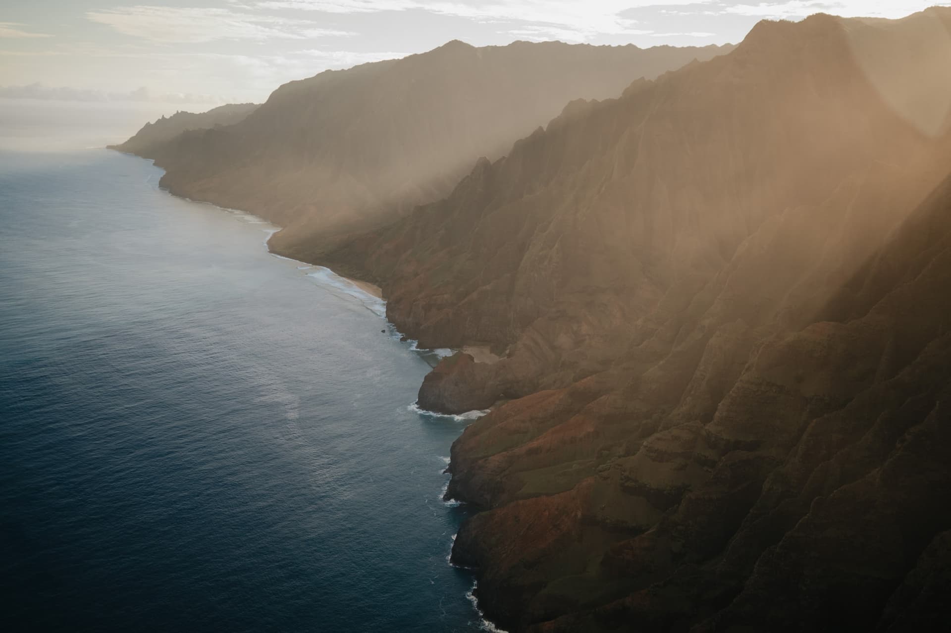 Sunlit coastal cliffs and turquoise ocean from above