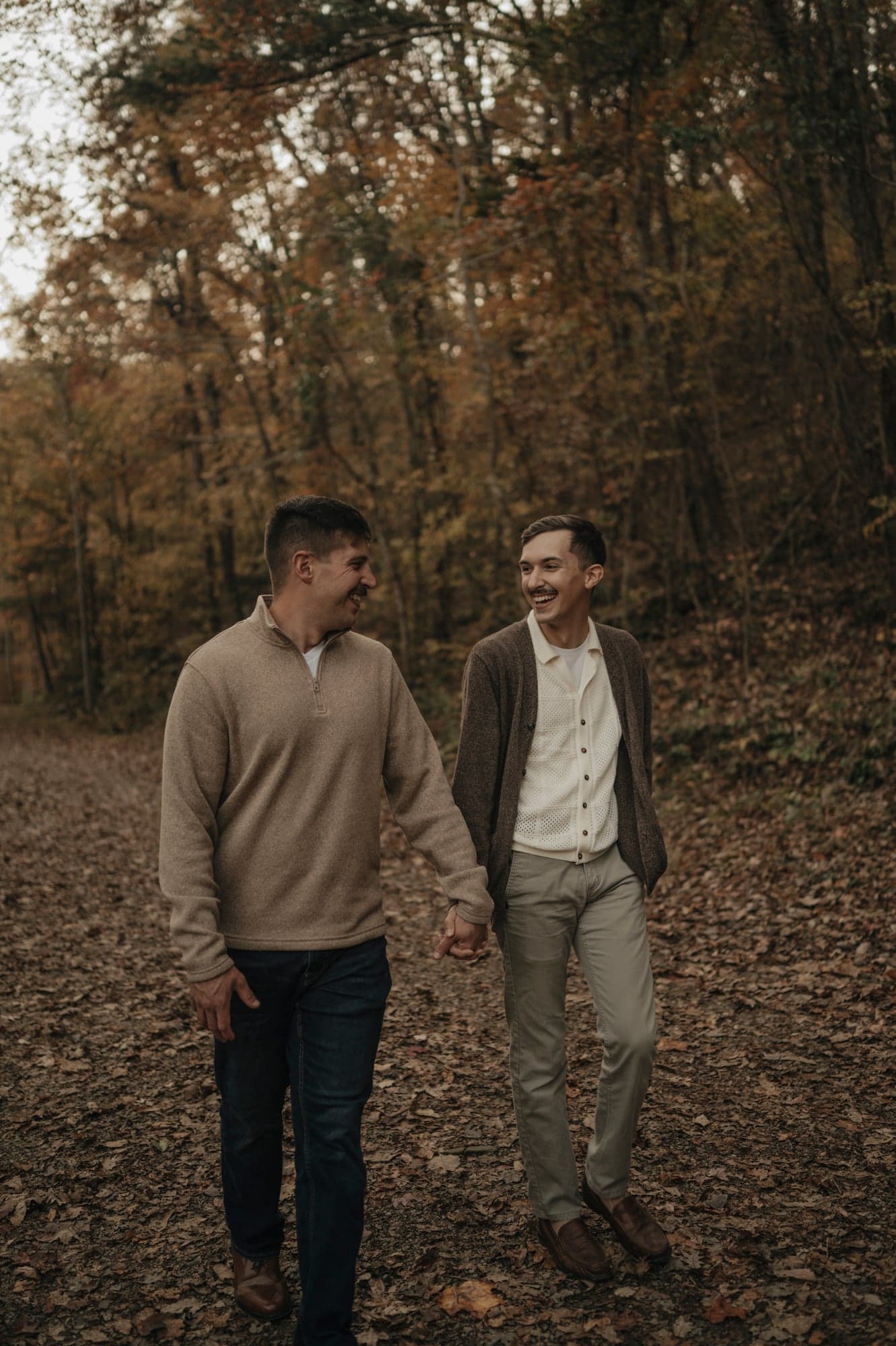 Couple walking through a leaf-covered forest path holding hands