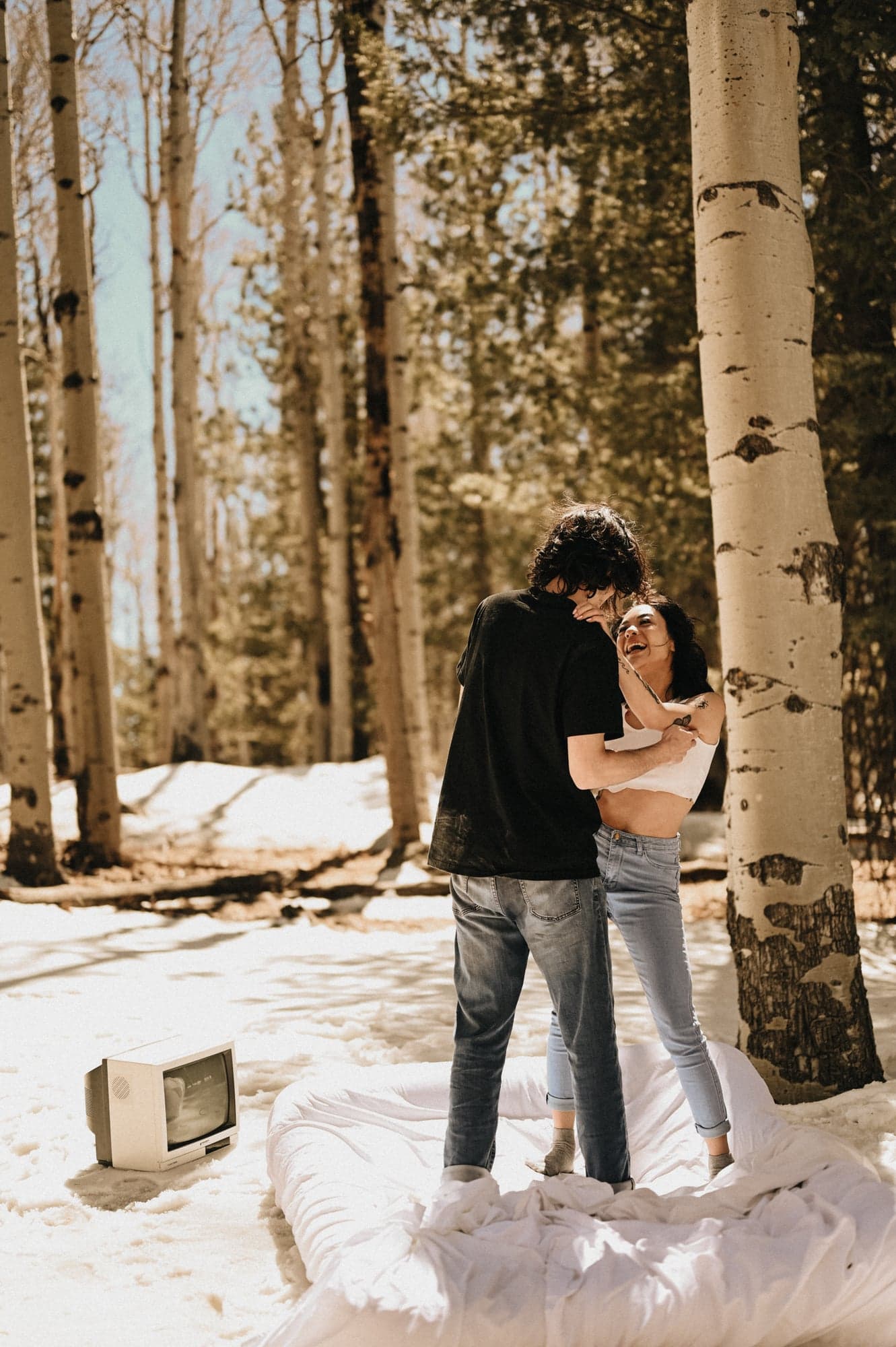 Couple laughing together on a mattress in a snowy aspen forest