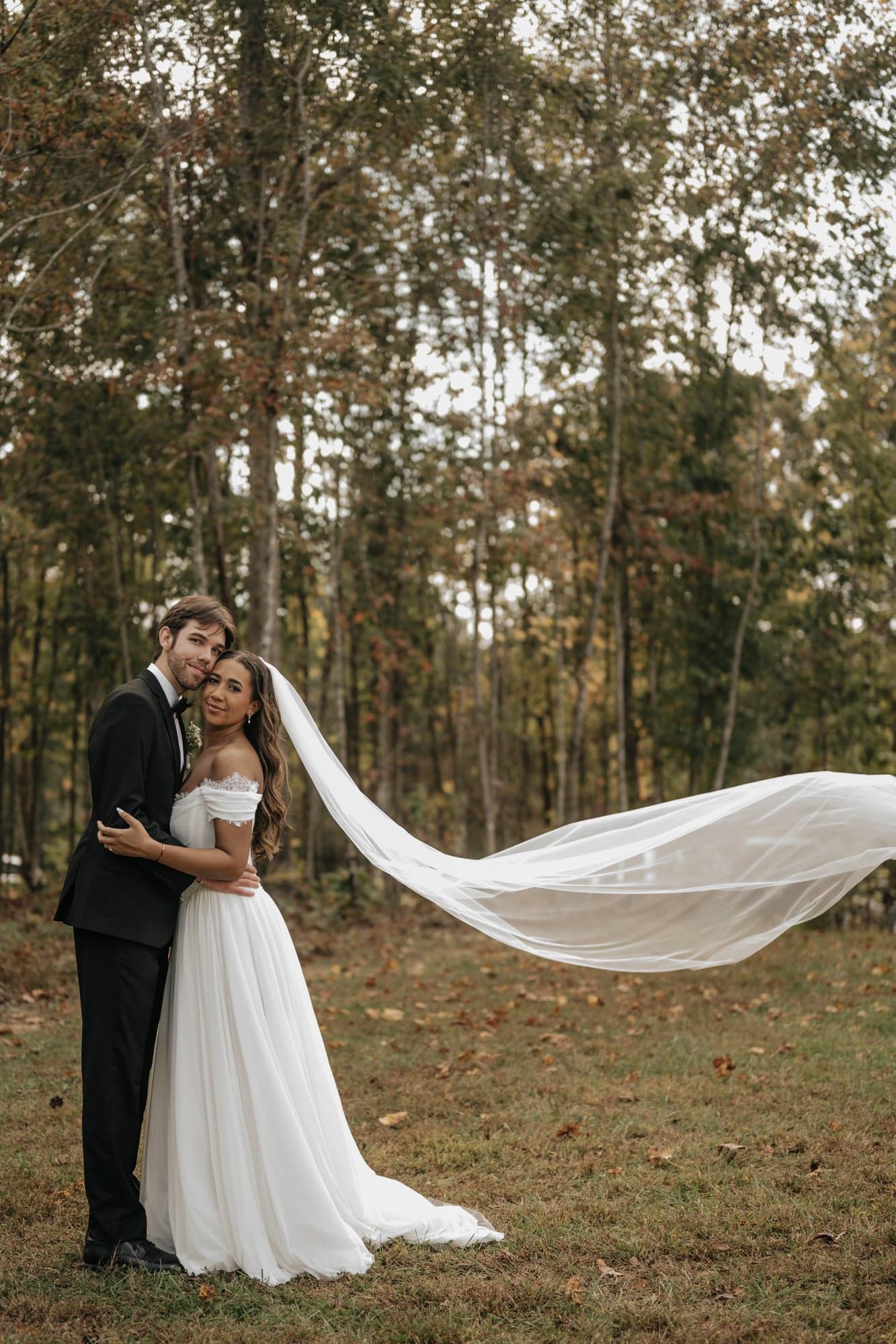 Bride and groom in the forest with a long veil flowing in the wind