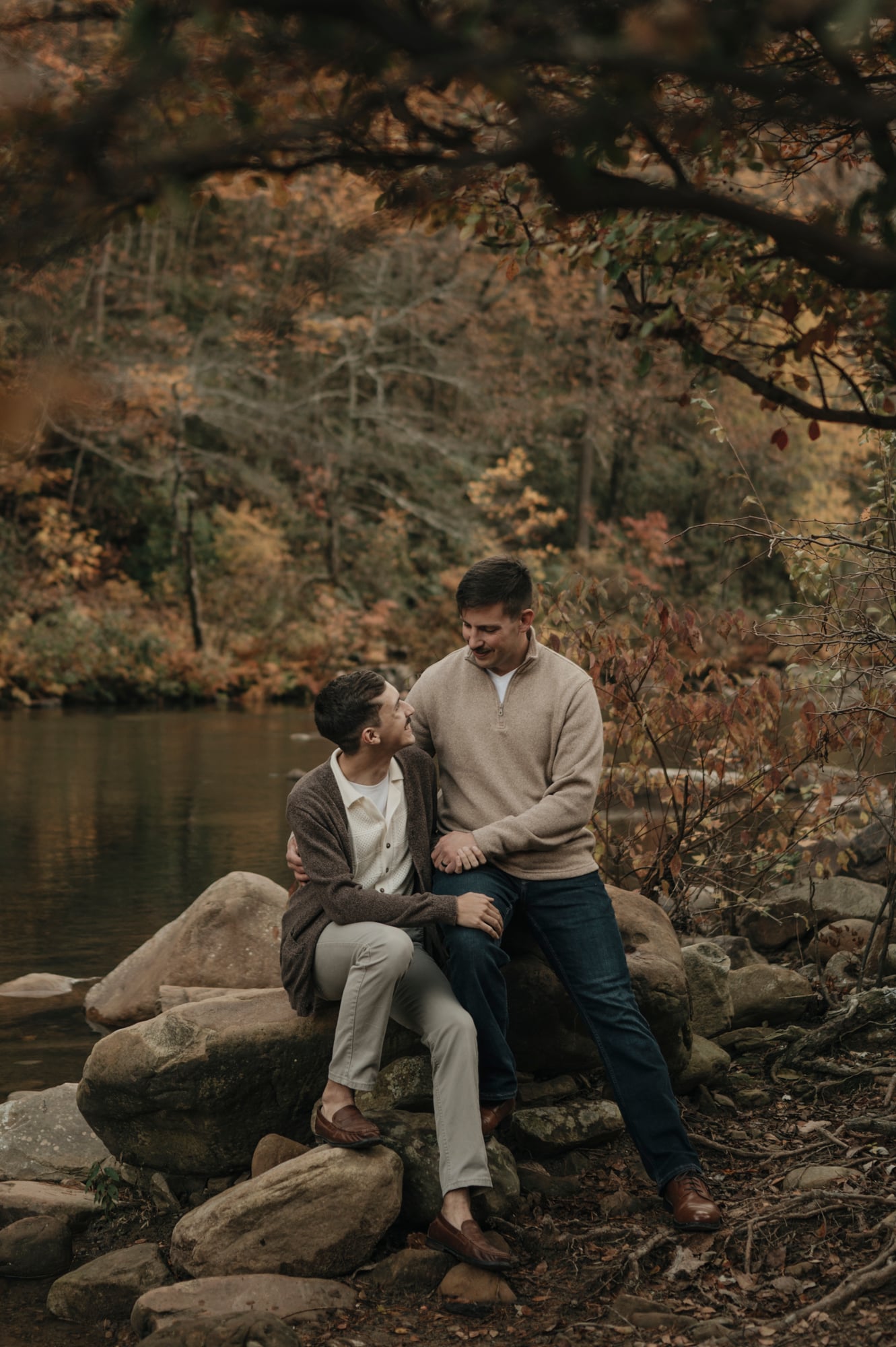 Couple sitting together on rocks beside a calm forest river