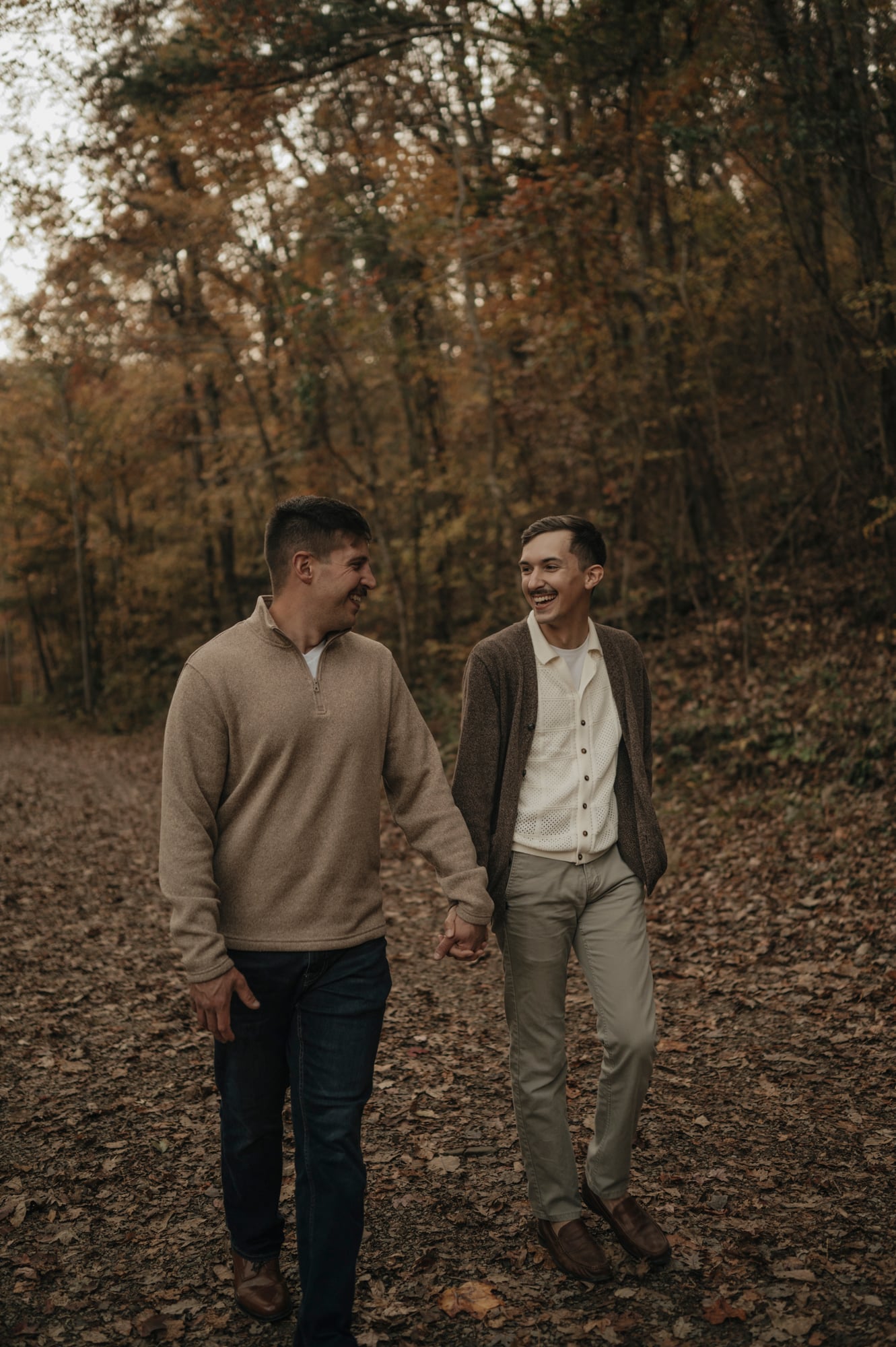 Couple walking through a leaf-covered forest path holding hands