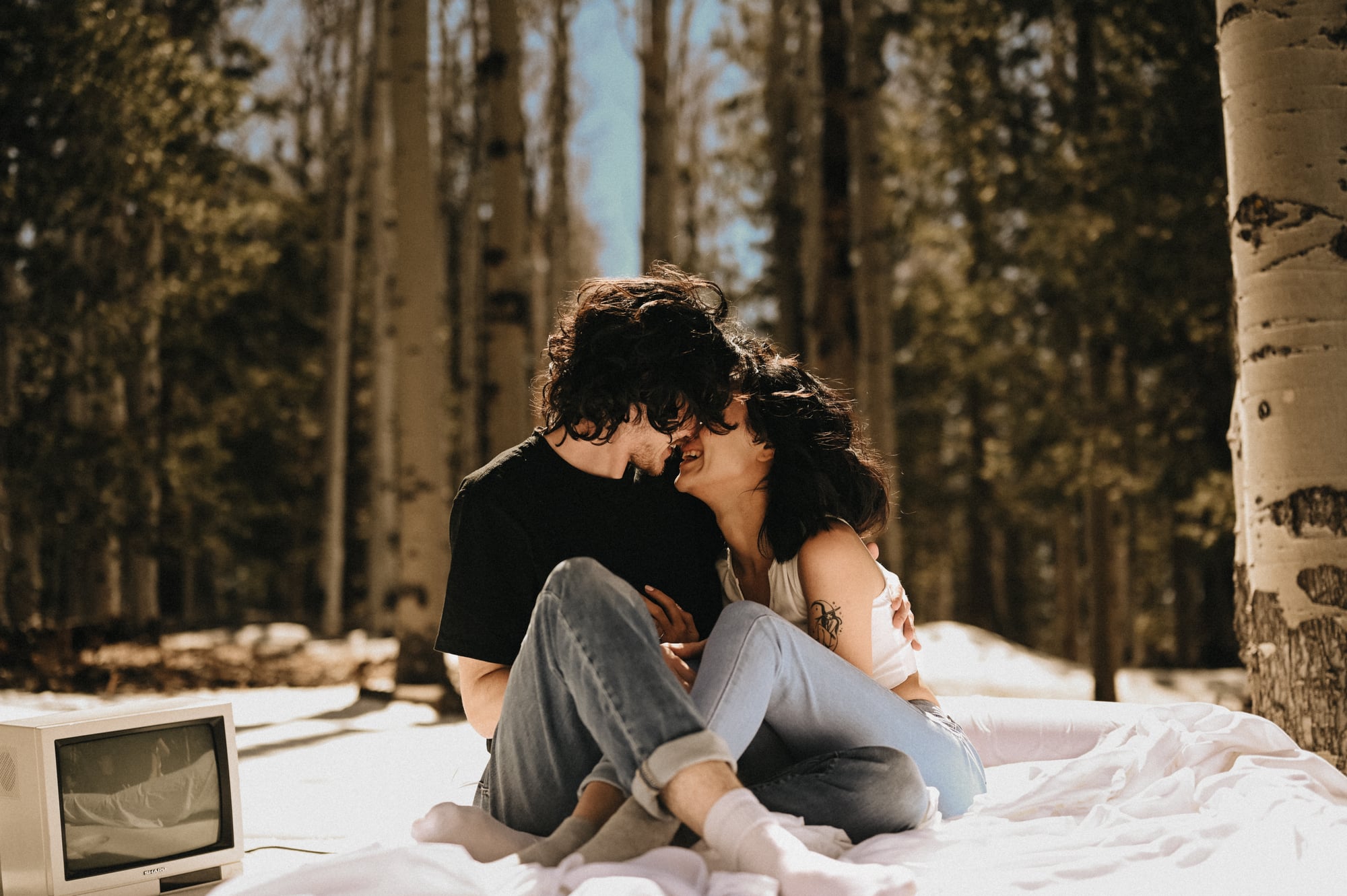 Couple sitting on a white blanket in the woods with foreheads touching