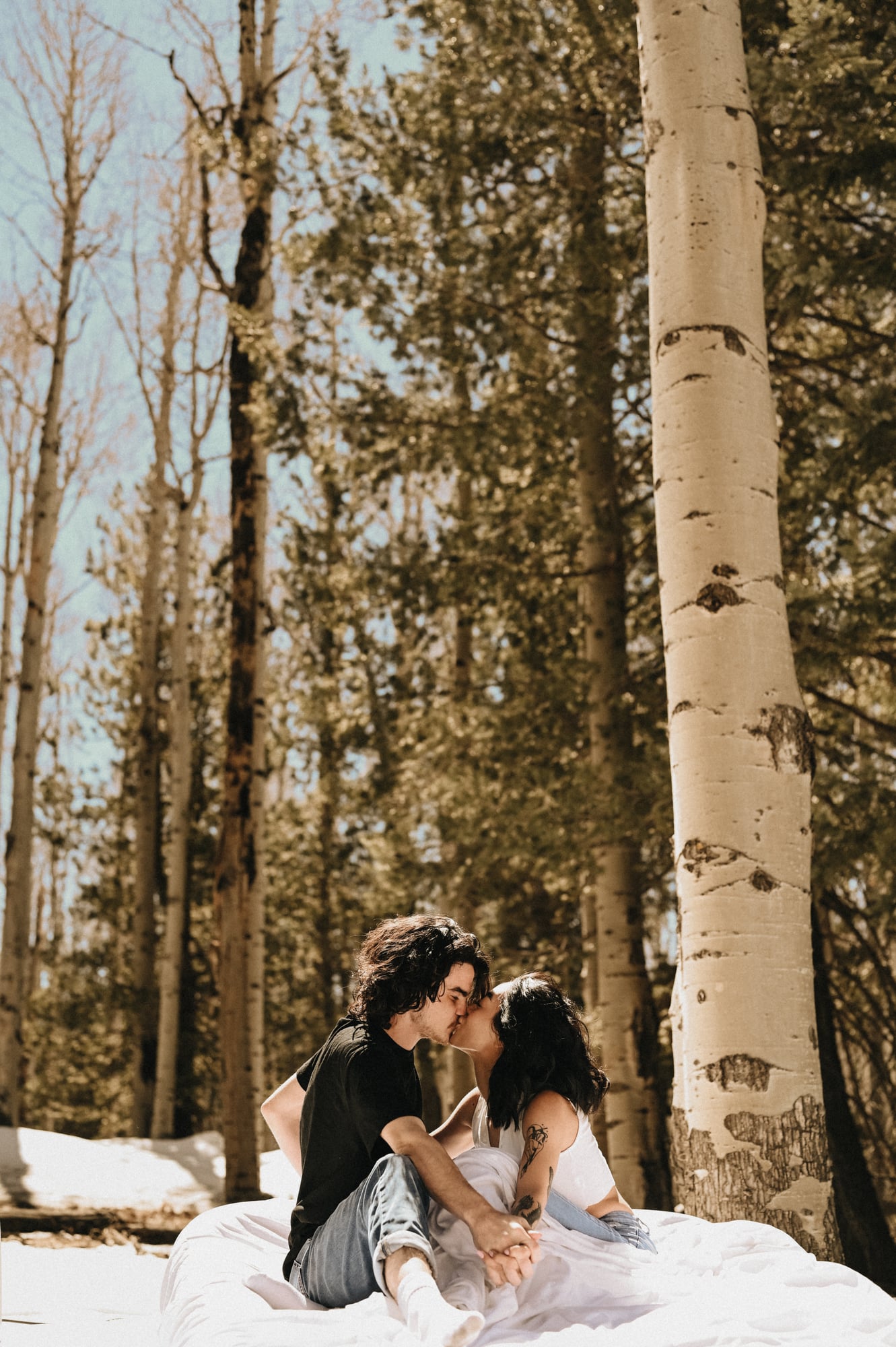 Couple sharing a kiss while seated on a white blanket in an aspen grove