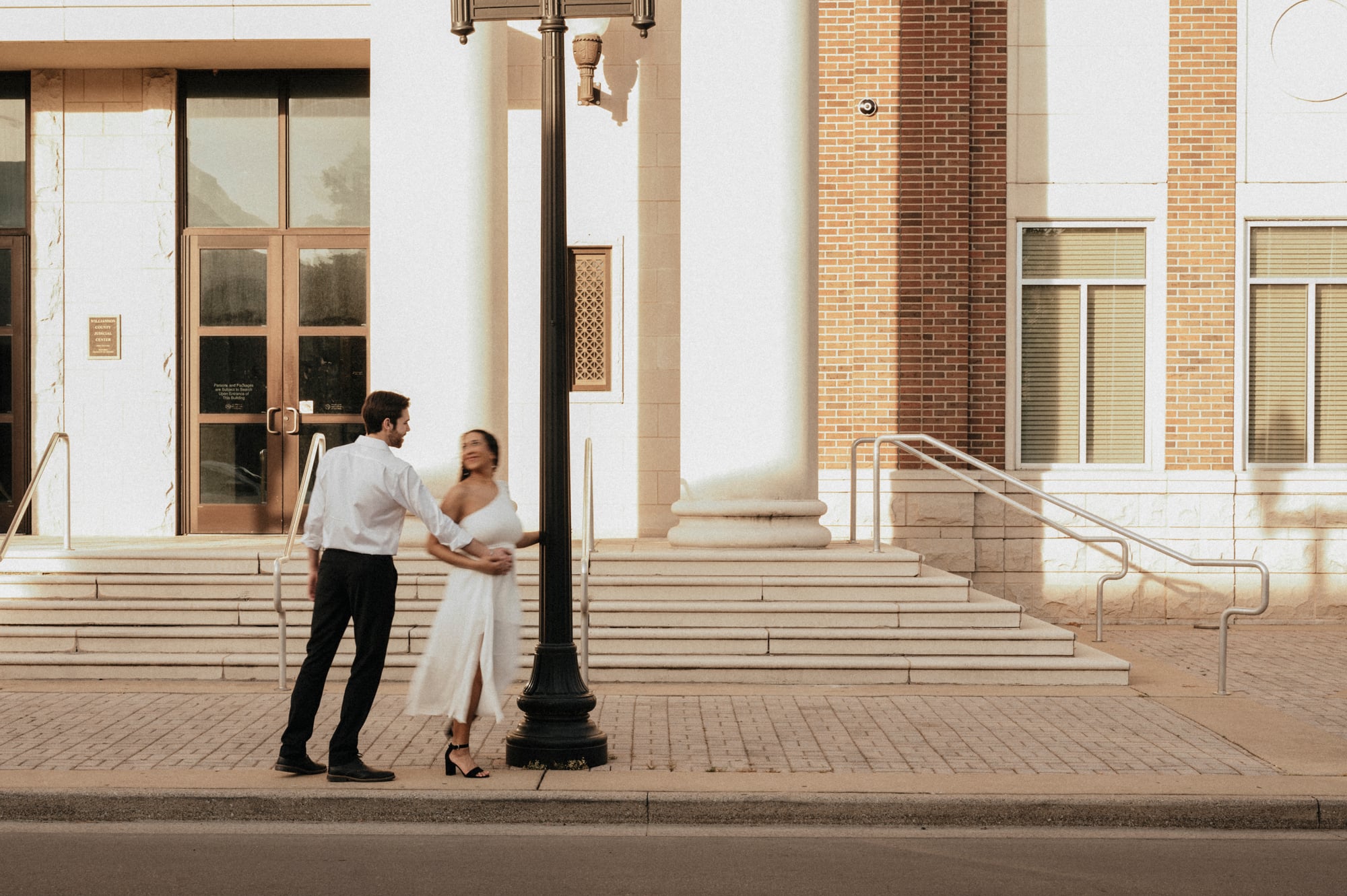 Couple standing together on the steps of a classical courthouse at golden hour