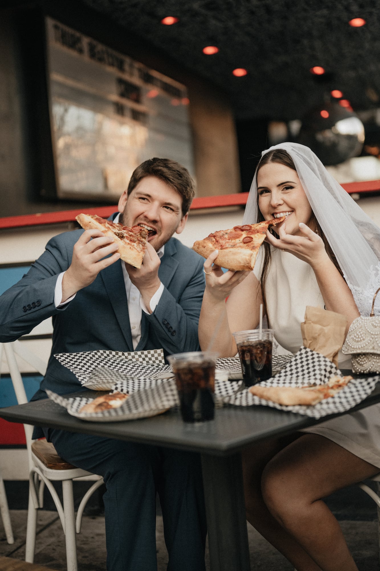 Bride and groom laughing while eating pizza together at night