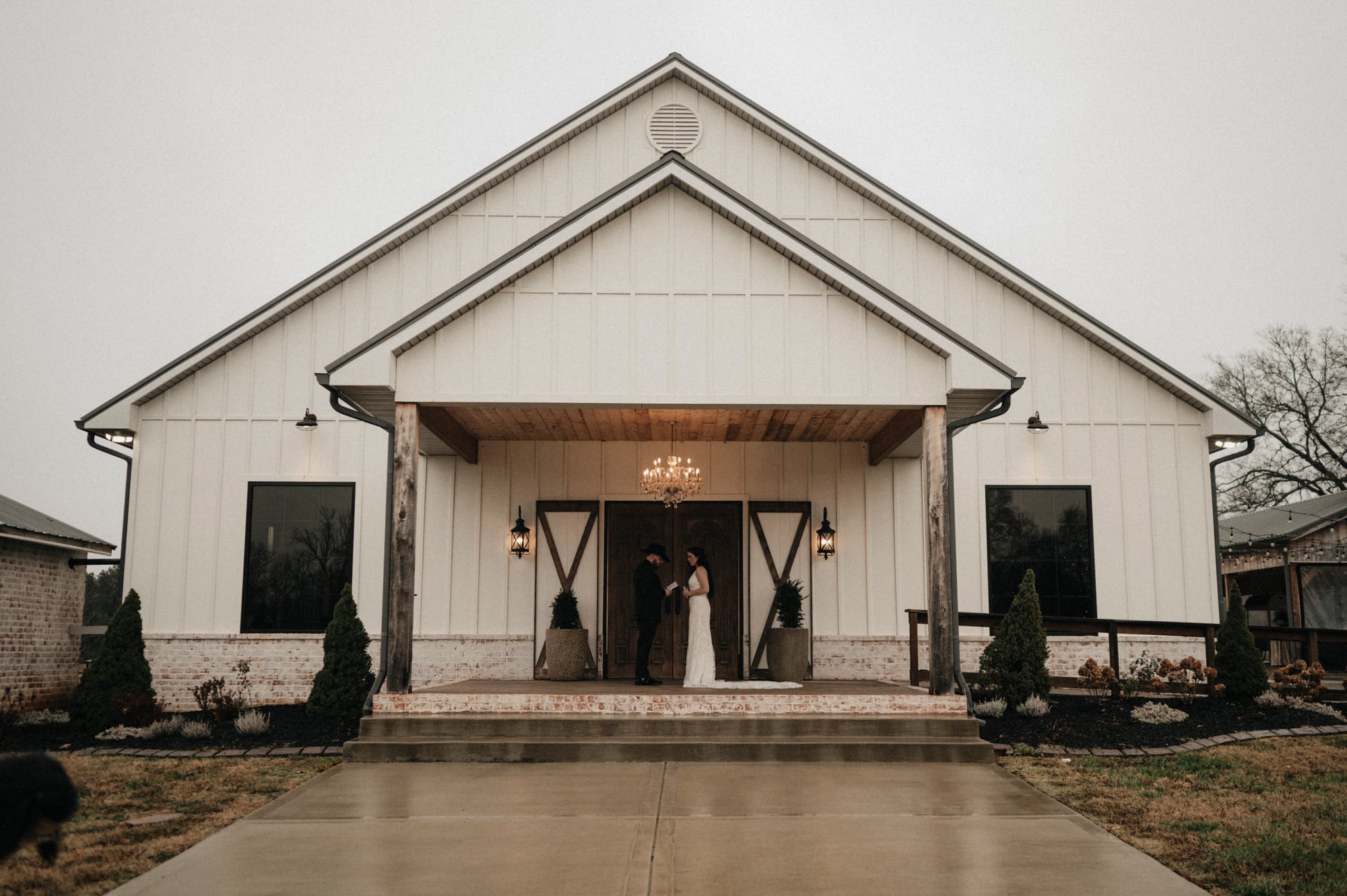 Bride and groom standing together on the porch of a white barn wedding venue