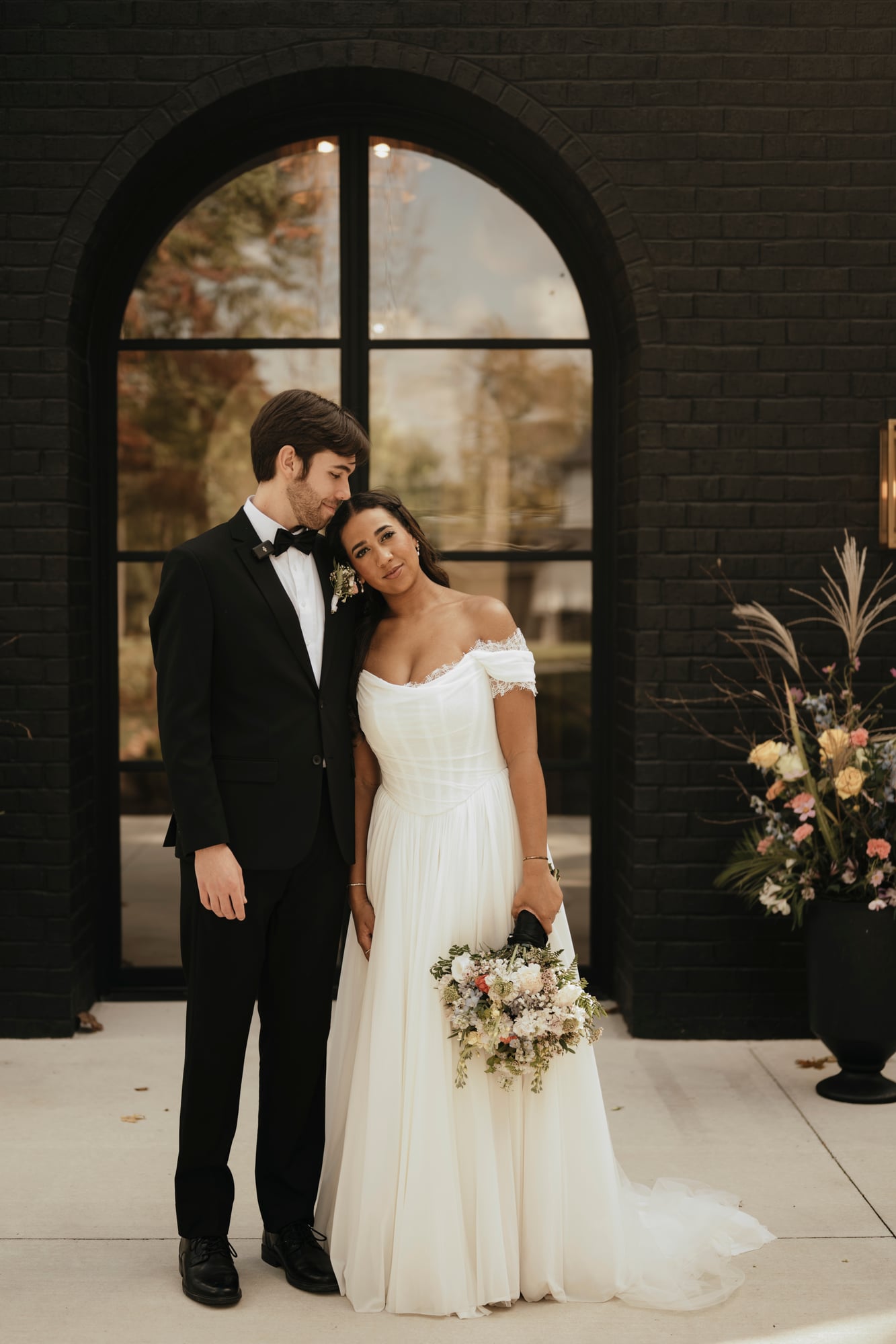 Bride and groom standing together in front of a black brick wall