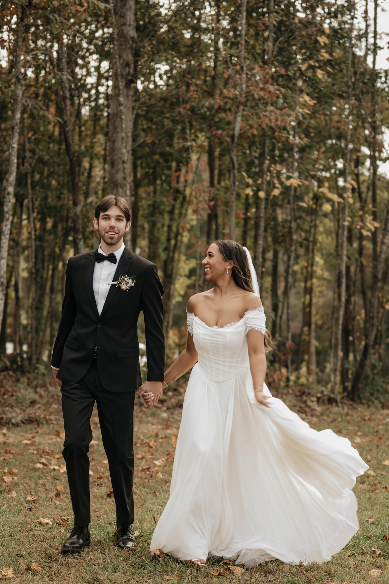 Bride and groom walking hand in hand through a wooded path