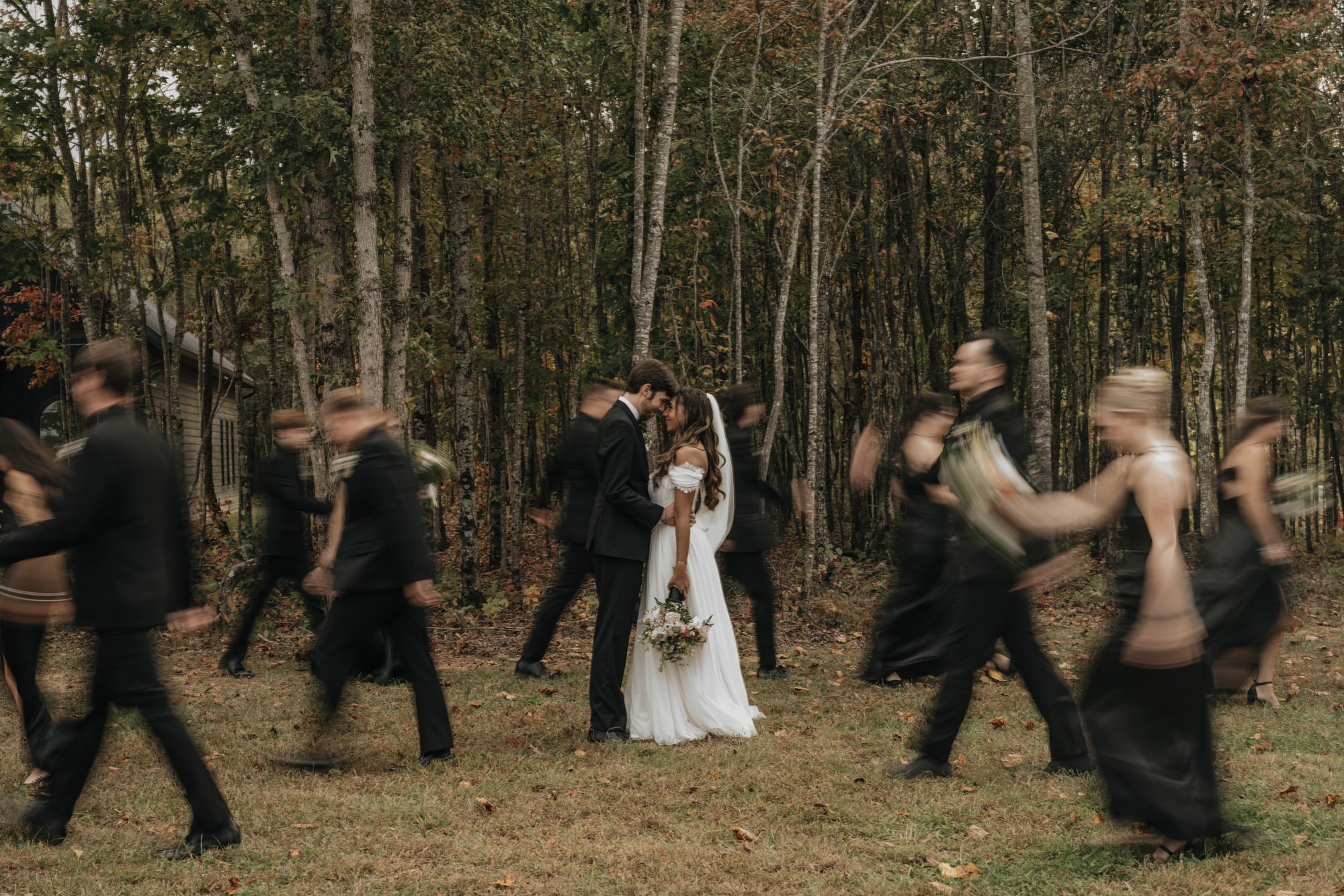 Bride and groom standing still as the wedding party rushes past around them