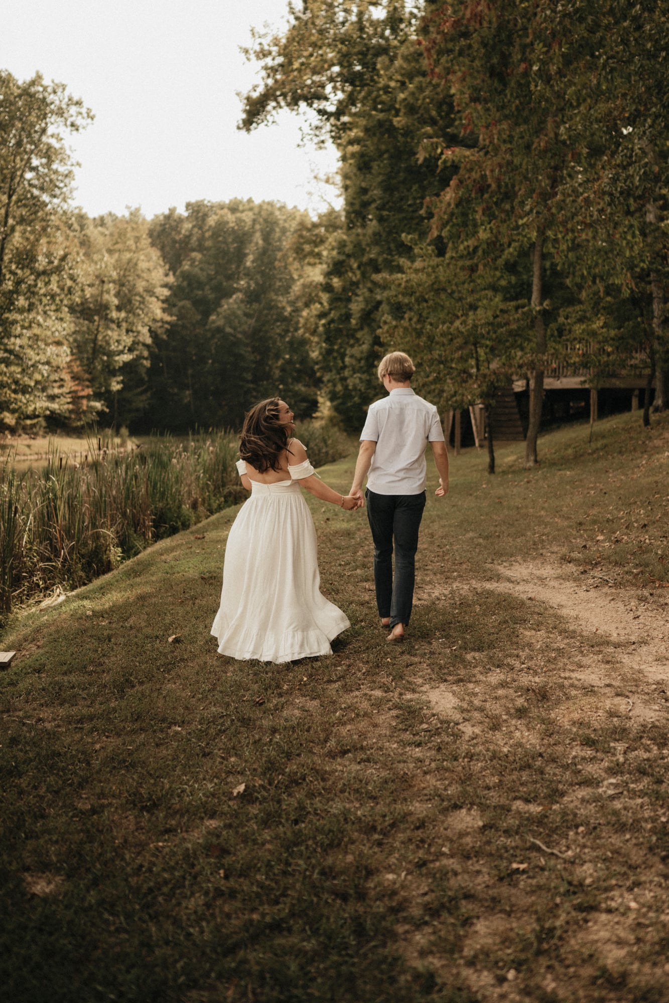 Couple walking hand in hand along a grassy path by the water