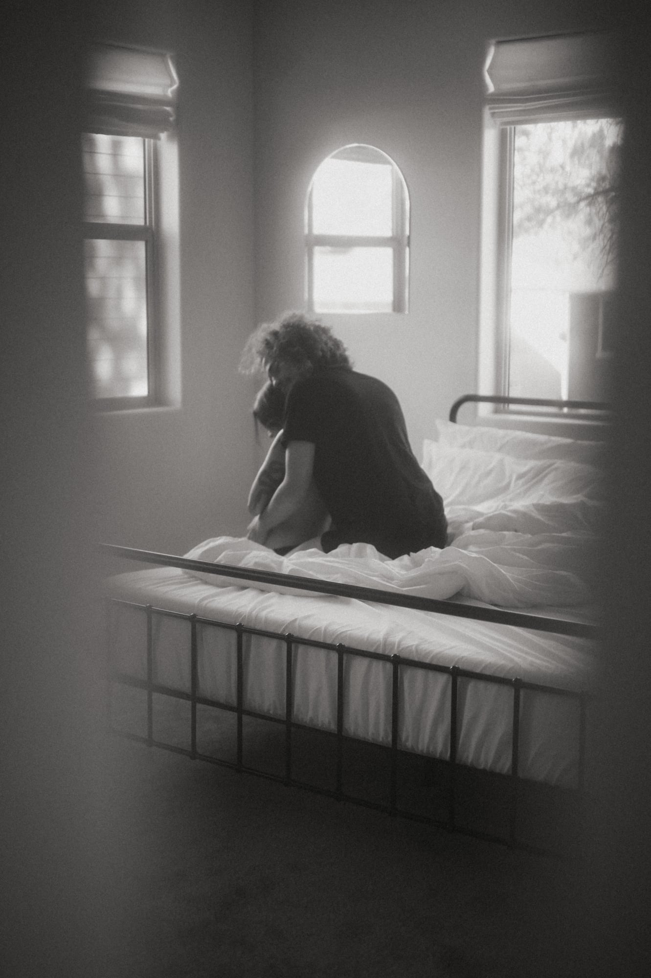 Black and white portrait of a couple embracing on a bed by sunlit windows