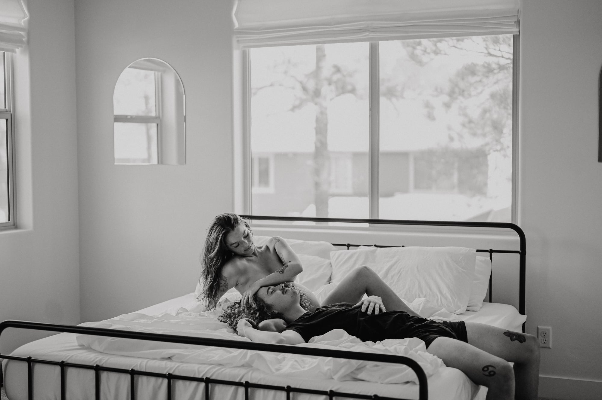 Black and white portrait of a couple lying together on white sheets