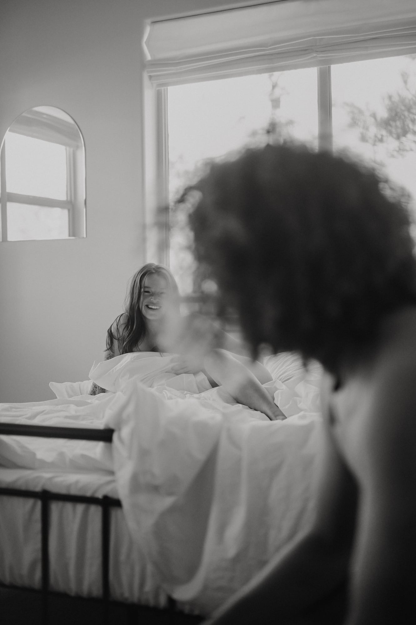 Black and white portrait of a woman laughing on a bed