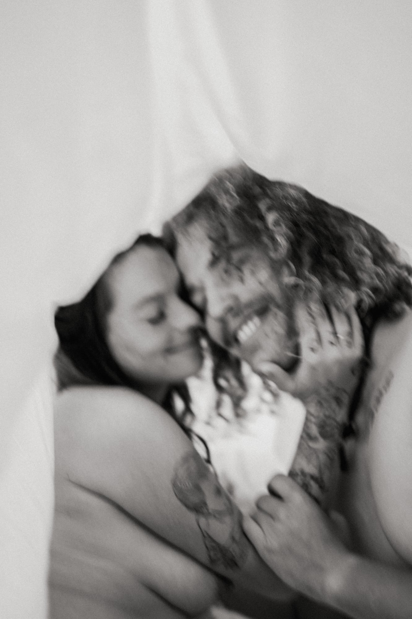 Black and white close-up of a couple smiling under white sheets