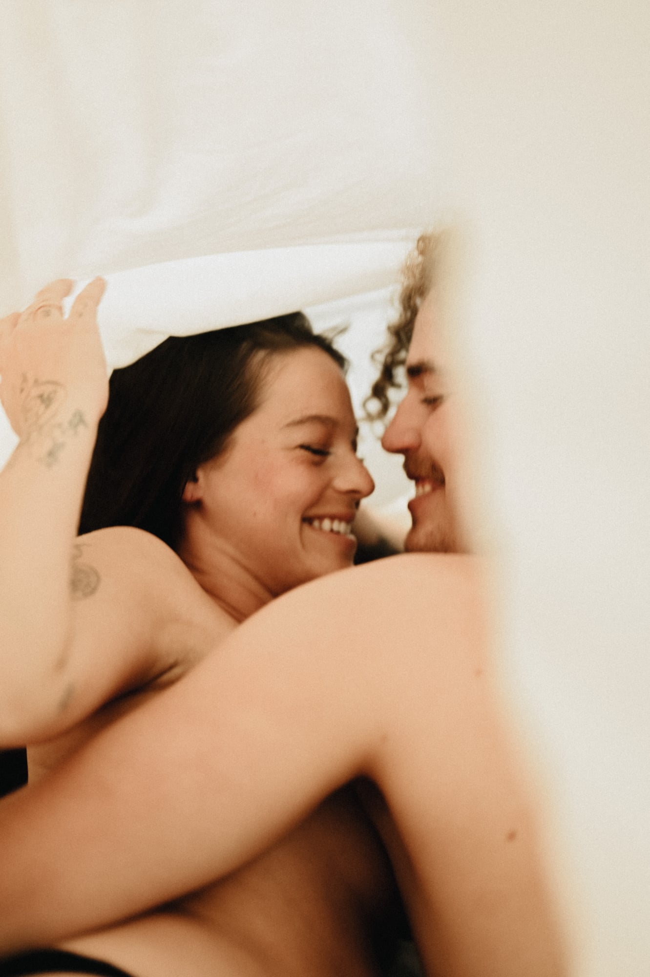 Couple laughing together under rumpled white bedsheets