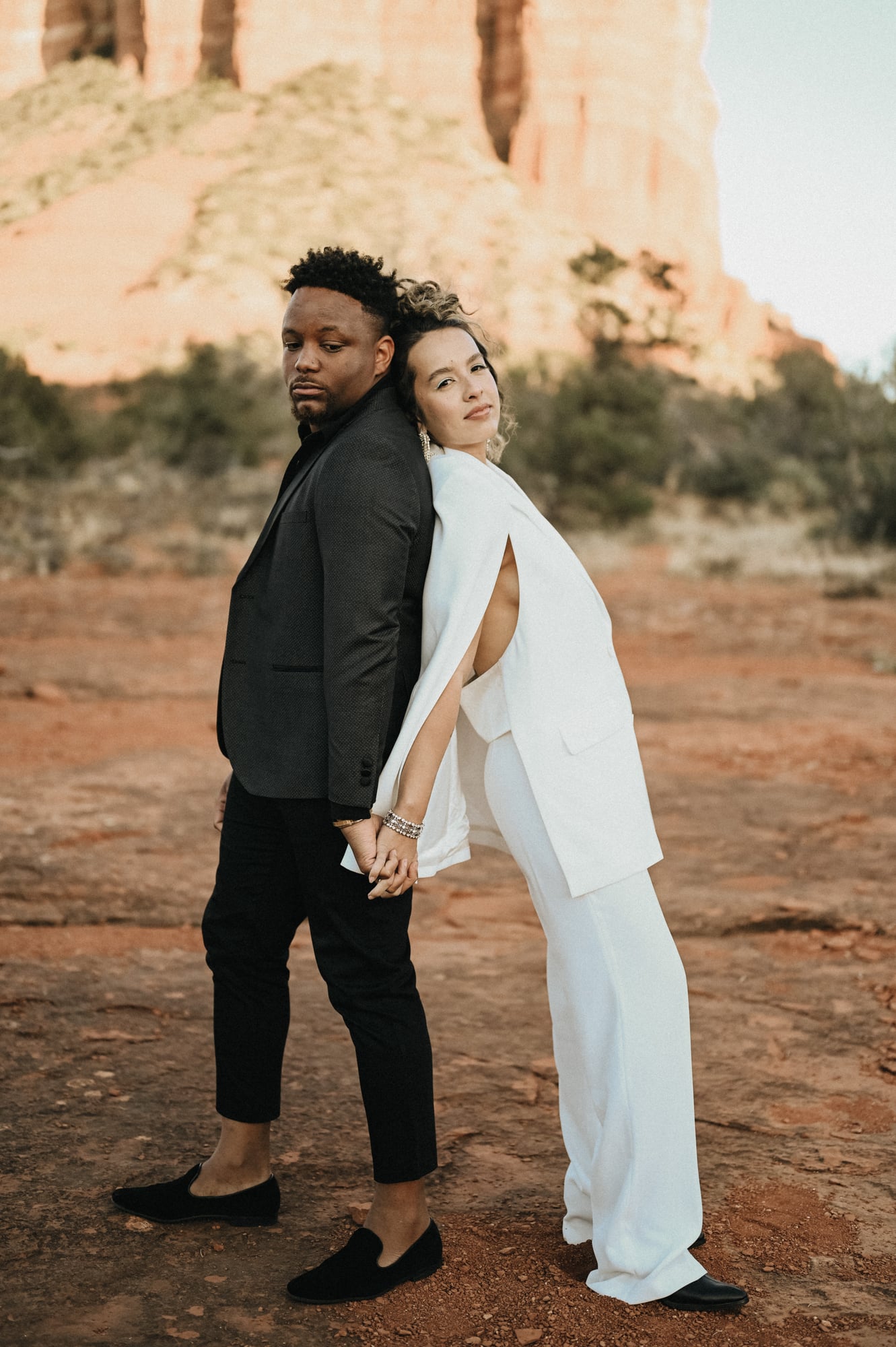 Couple standing back to back in the Sedona desert wearing white suits