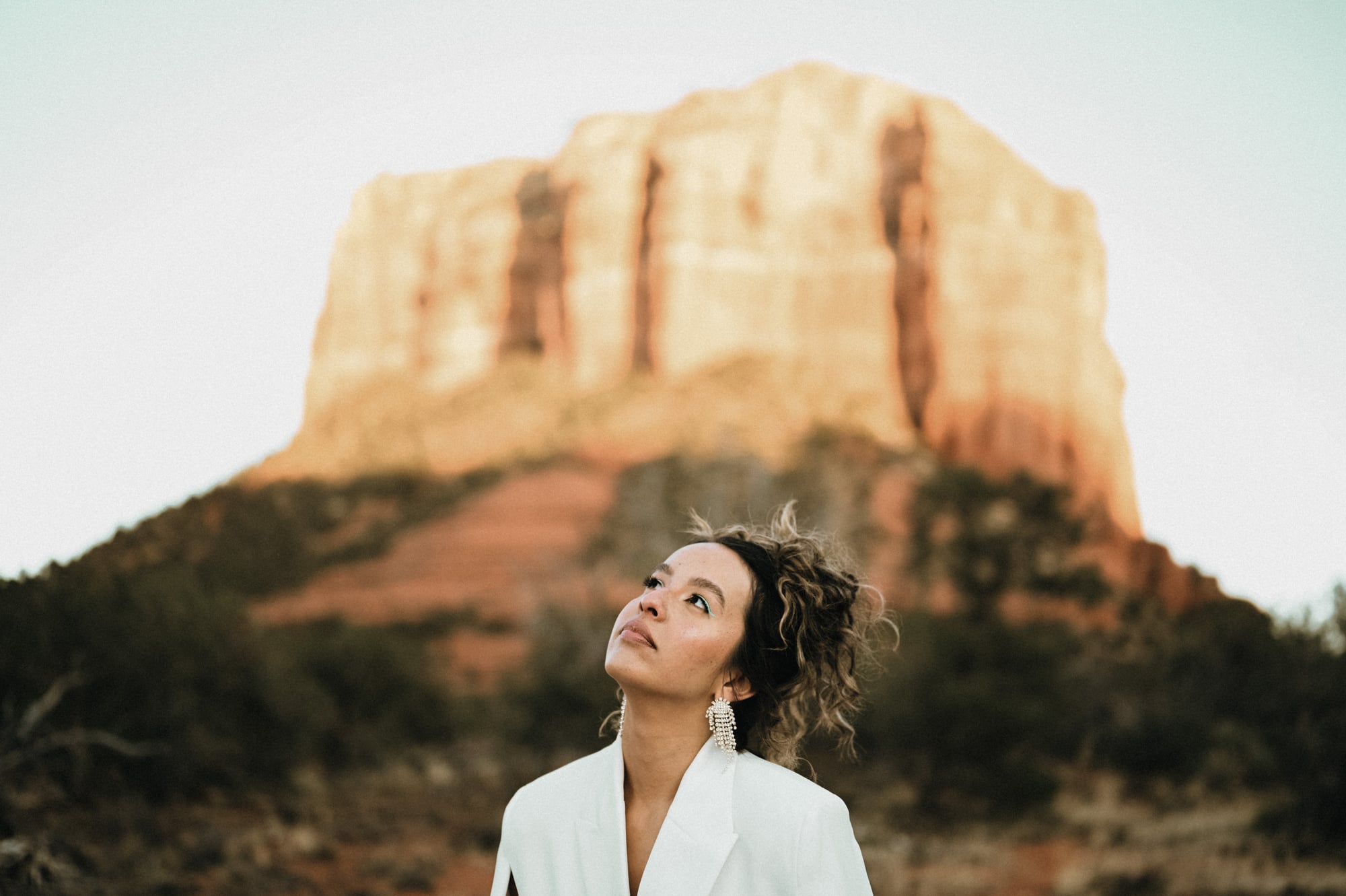 Woman in a white blazer looking up toward a red rock butte in Sedona